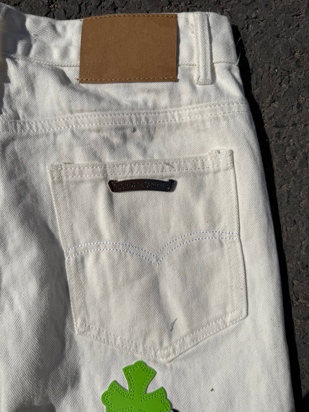 White denim pants back view with waistband tag and large green cross applique