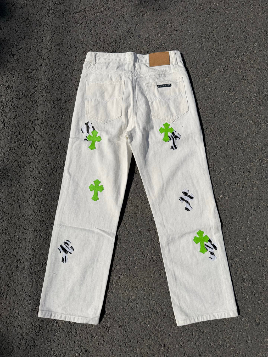 White denim pants with back yoke, green cross patches, and black graphic marks
