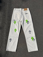 White denim pants with back yoke, green cross patches, and black graphic marks