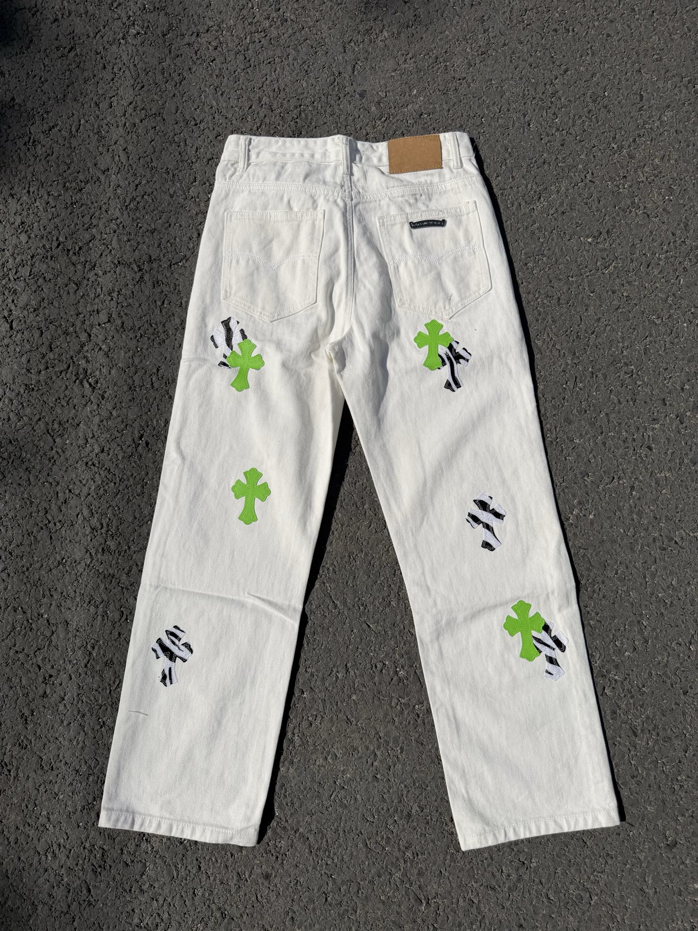 White denim pants with back yoke, green cross patches, and black graphic marks