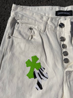 White denim pants close-up of buttoned waistband and green cross applique with black detail