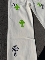 White denim pants side view with green cross patches and black graphic artwork