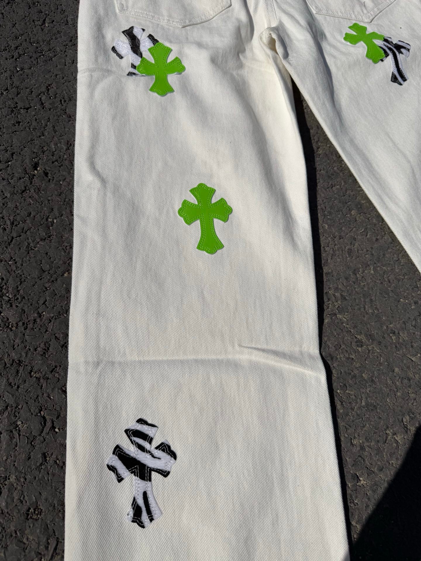 White denim pants side view with green cross patches and black graphic artwork