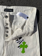 White denim pants with label tab, button closure, and green cross patch on front pocket