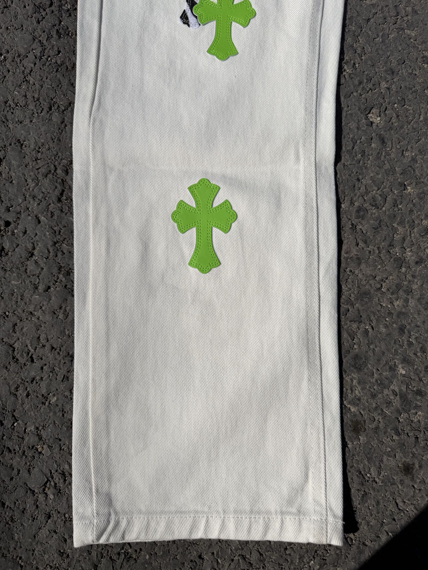 White denim pants leg with green cross patch print and smooth stitched front panel