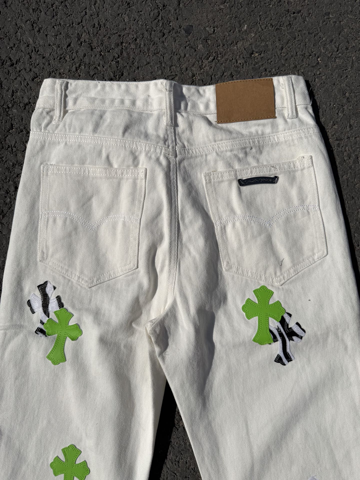 White denim pants with front pockets and green cross patches with black graphic accents