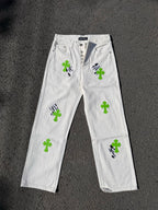 White denim pants with button fly, green cross patches, and black graphic details