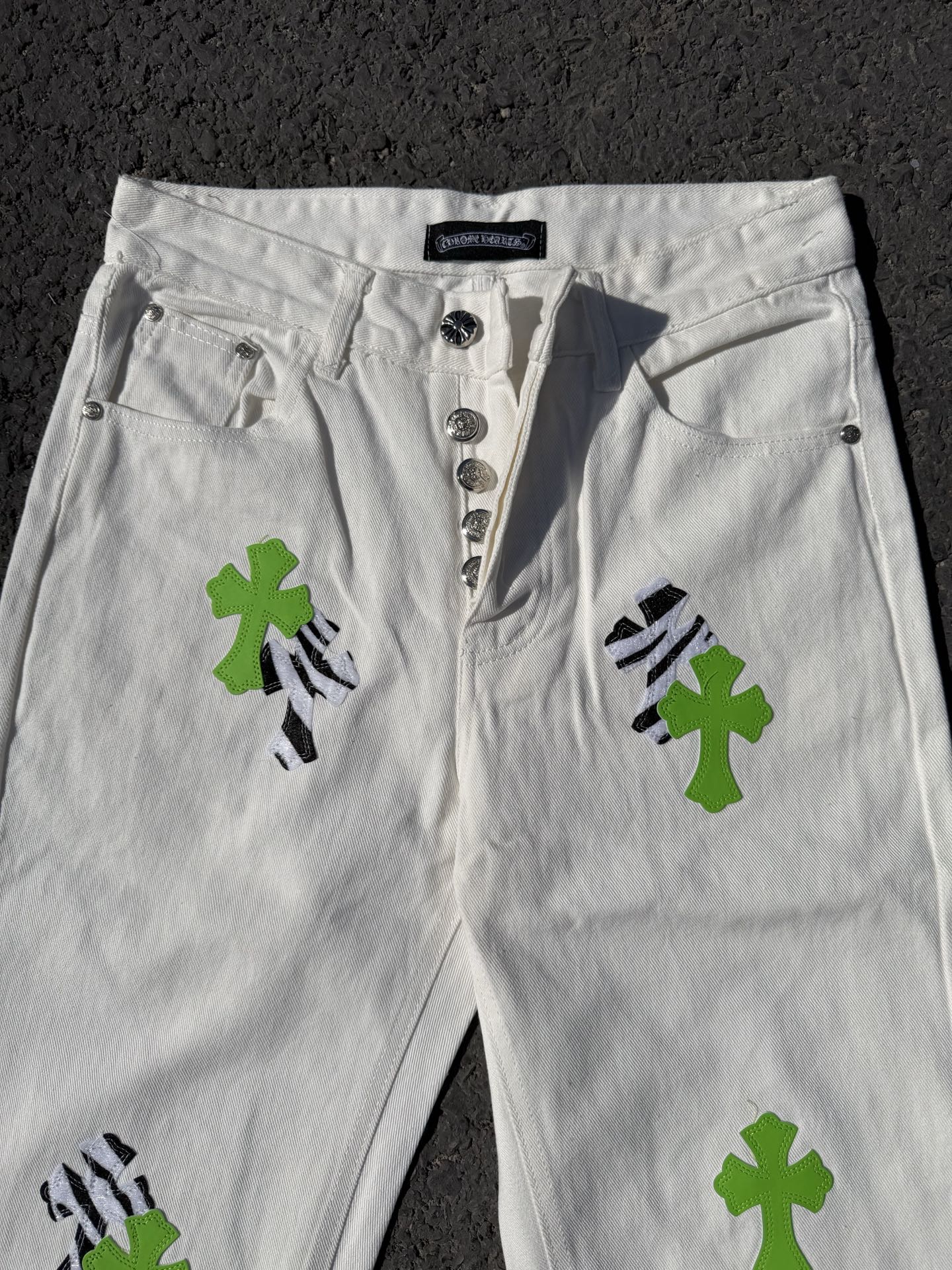 White denim pants with front button placket and green cross patches with black accents