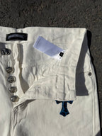 White pants with button fly, front pocket, and orange/blue cross design near hem