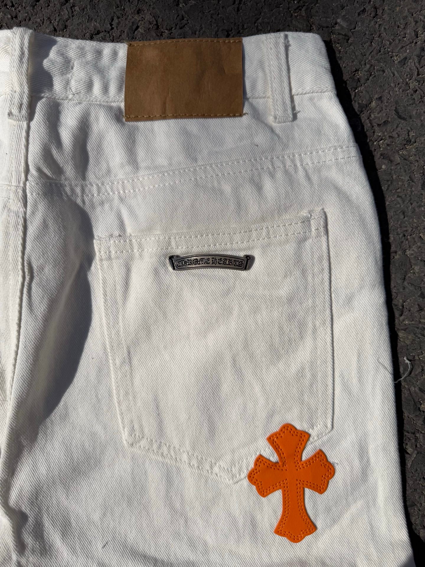 White pants with back pocket, belt loops, and orange cross graphic on the thigh