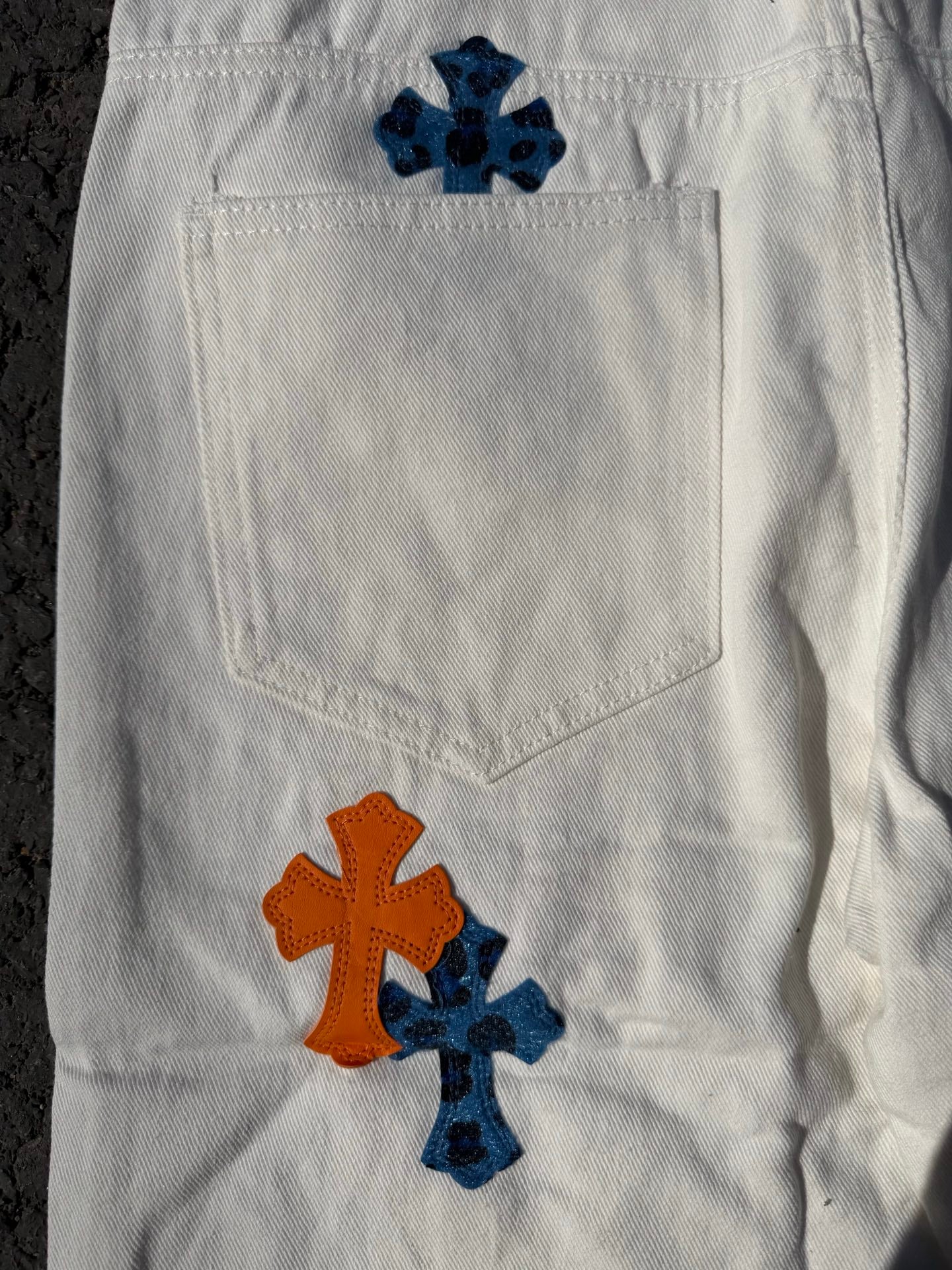 White pants with large orange and blue cross print on one leg and back pocket
