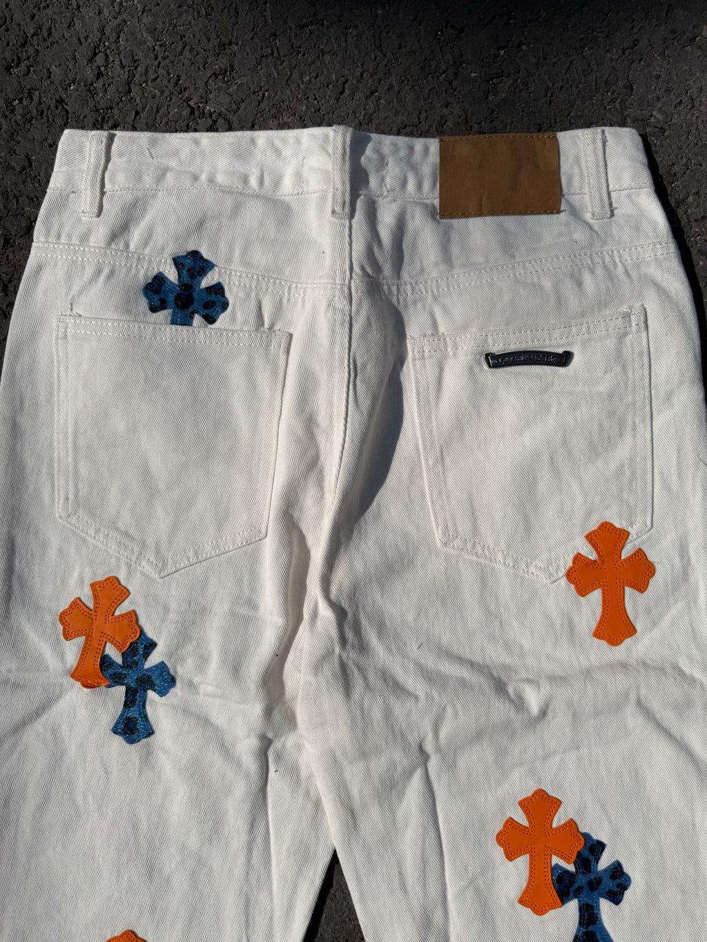 White cross-print pants with side pockets and orange/blue graphics on both legs