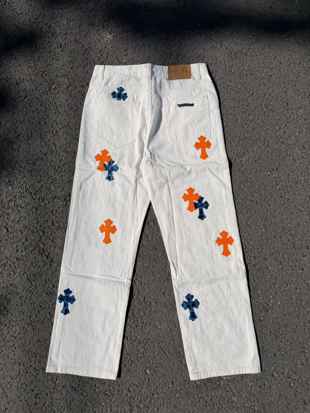 White pants with repeated orange and blue cross graphics, fly front and side pockets