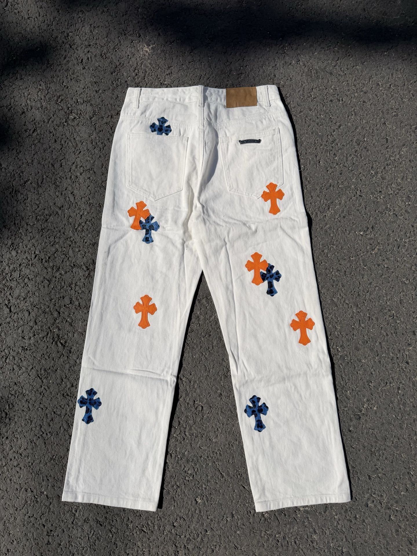 White pants with repeated orange and blue cross graphics, fly front and side pockets