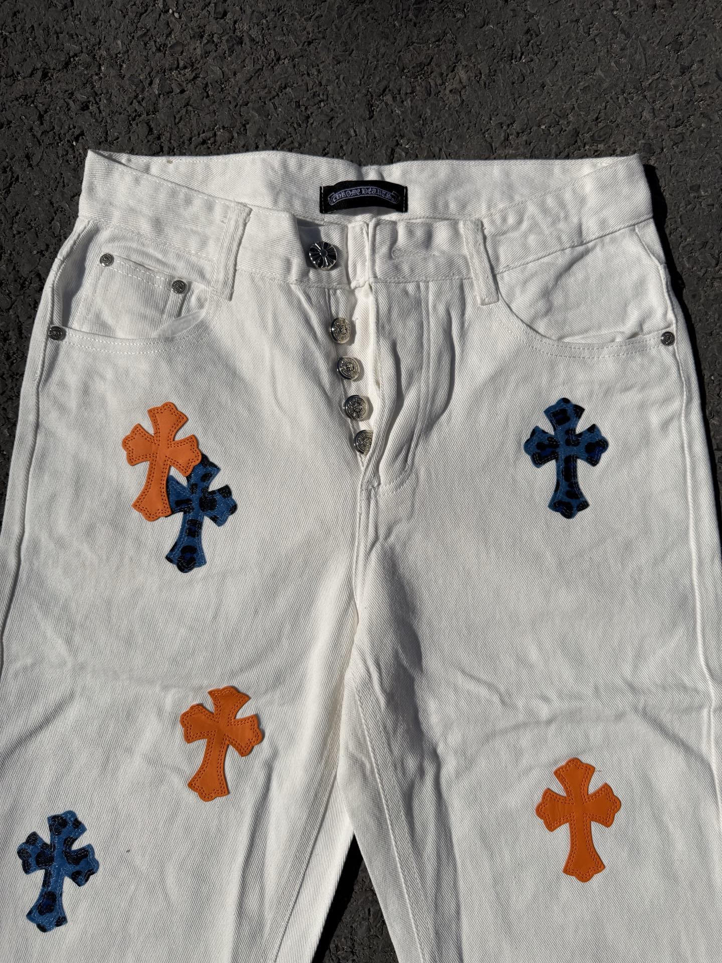 White cross-print pants with button fly, belt loops, and front pocket details