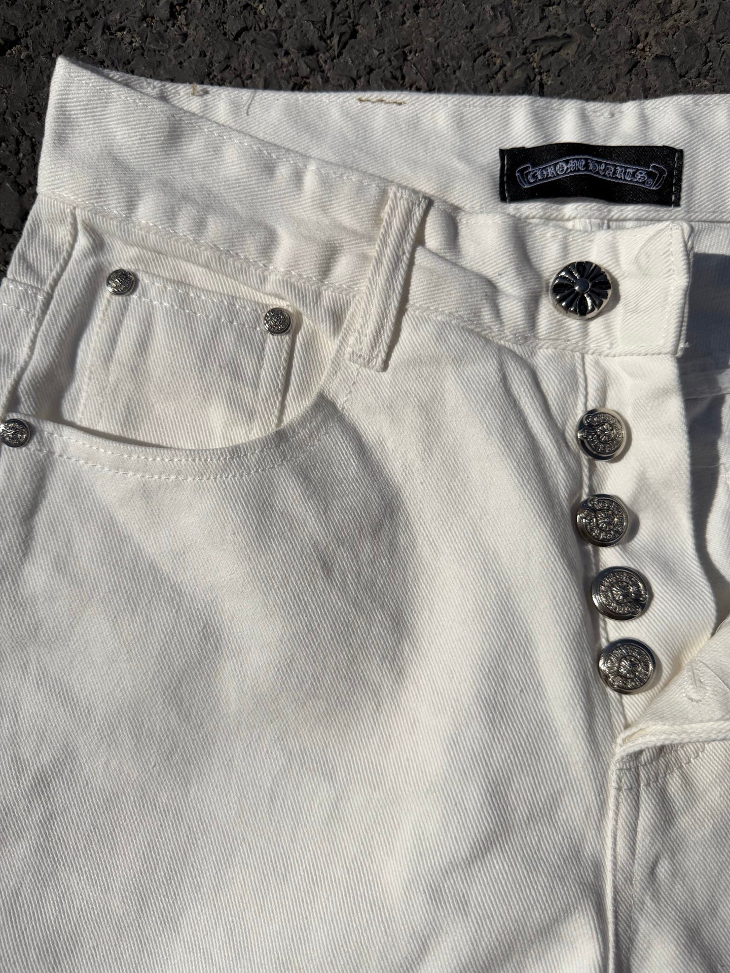 White denim pants with front pockets and dark button details near the waistband