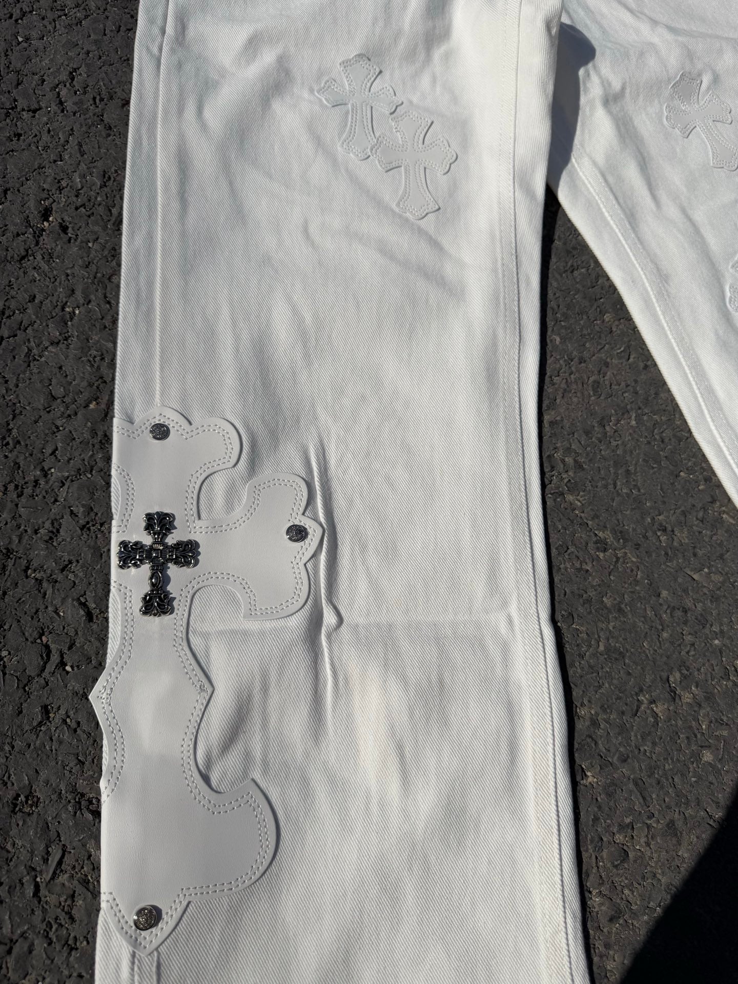 White denim pants with small embroidered floral motifs and button details