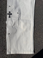White denim pants with side embroidery and dark button accents along the hem