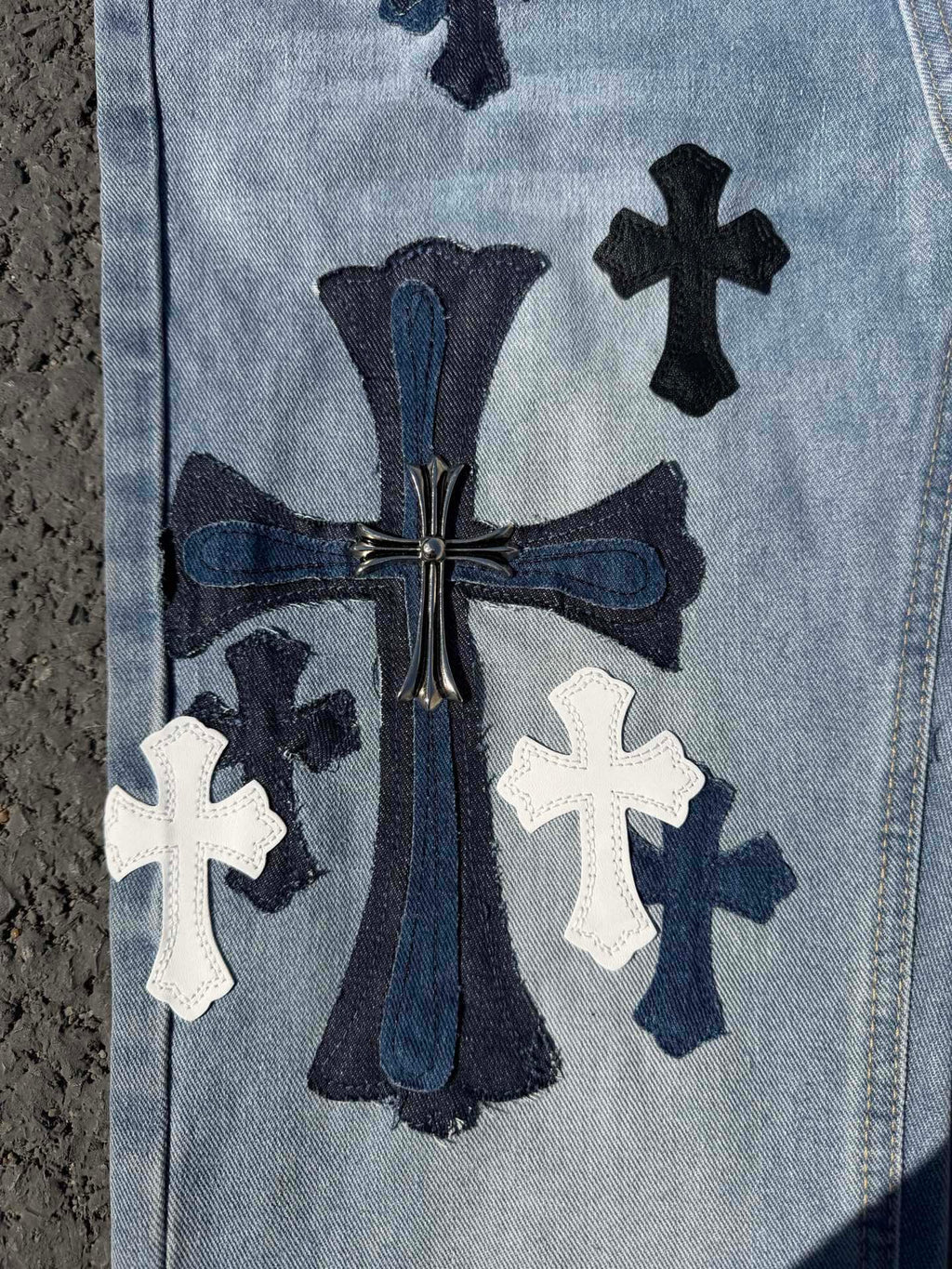 Light wash denim pants with ornate center graphic and white cross patches