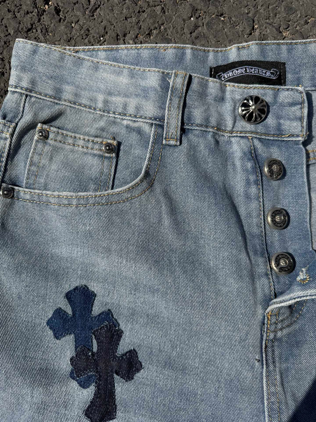 Light wash denim pants with front button placket and navy cross patch on pocket