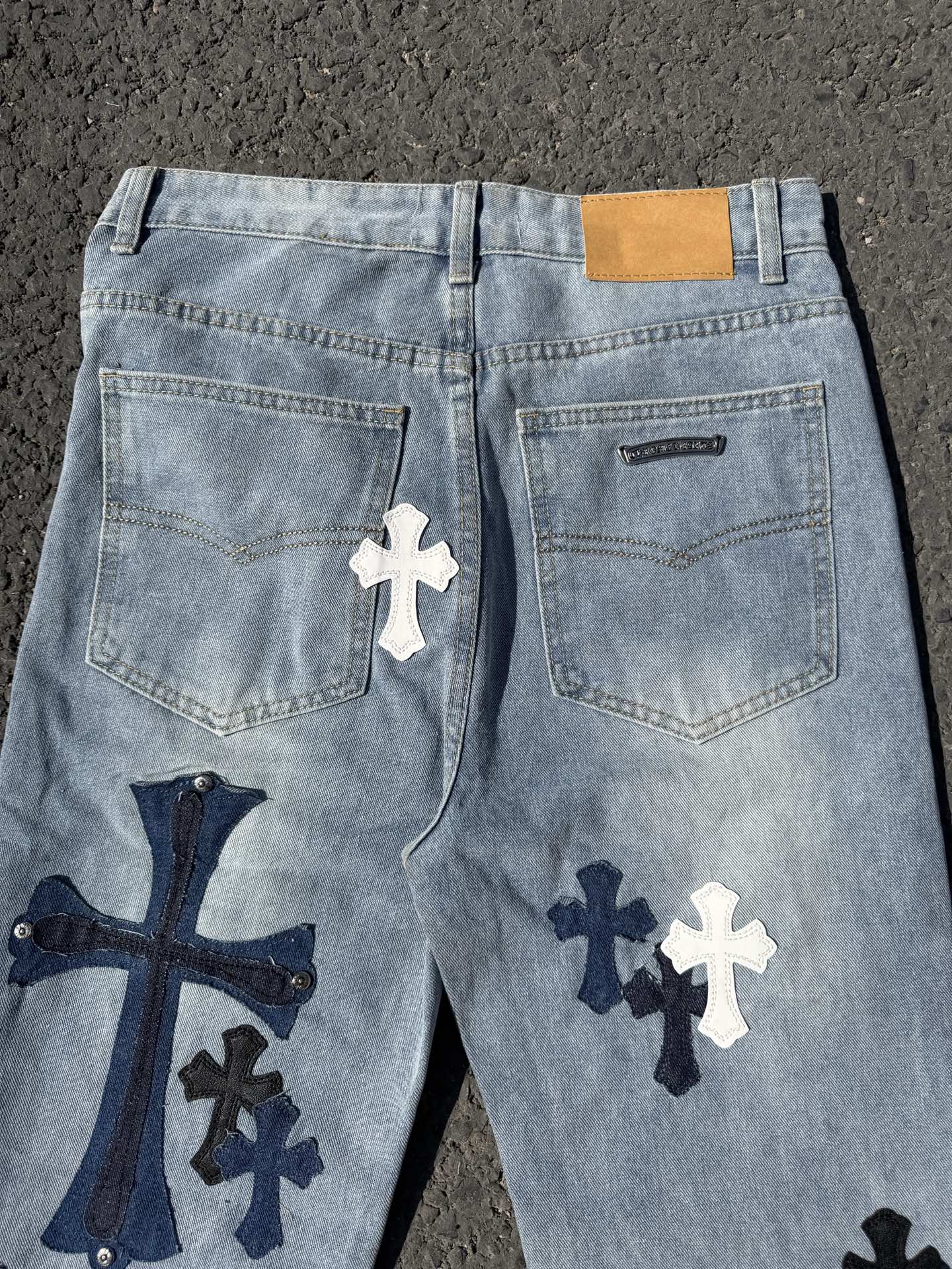 Light wash denim pants with front pockets, logo tab, and cross graphics