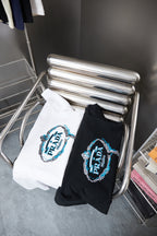 Two folded Prada T-shirts on rack: white and black with embroidered PRADA logos