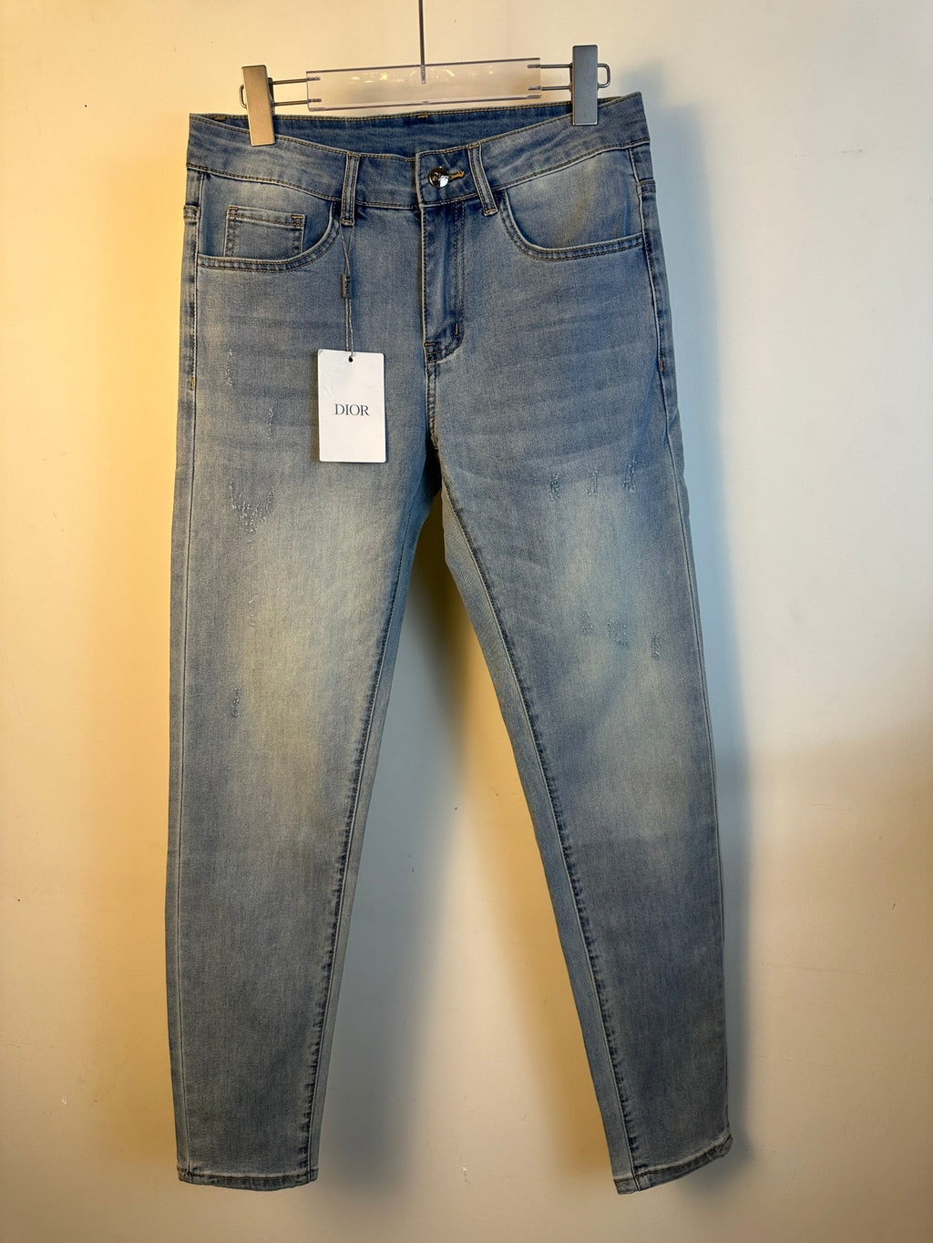 Light blue wash denim jeans with five pockets and belt loops, hanging tag on waist.