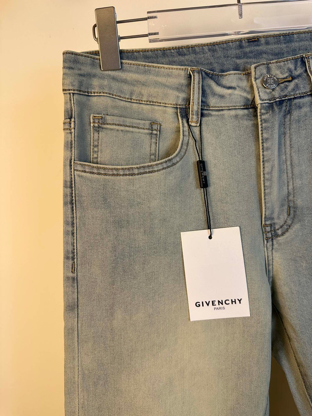 Givenchy light-wash denim jeans close-up at waist with front pockets and hanging tag