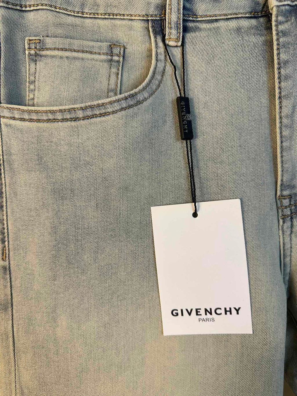 Light-wash denim jeans close-up of front pocket with hanging Givenchy tag