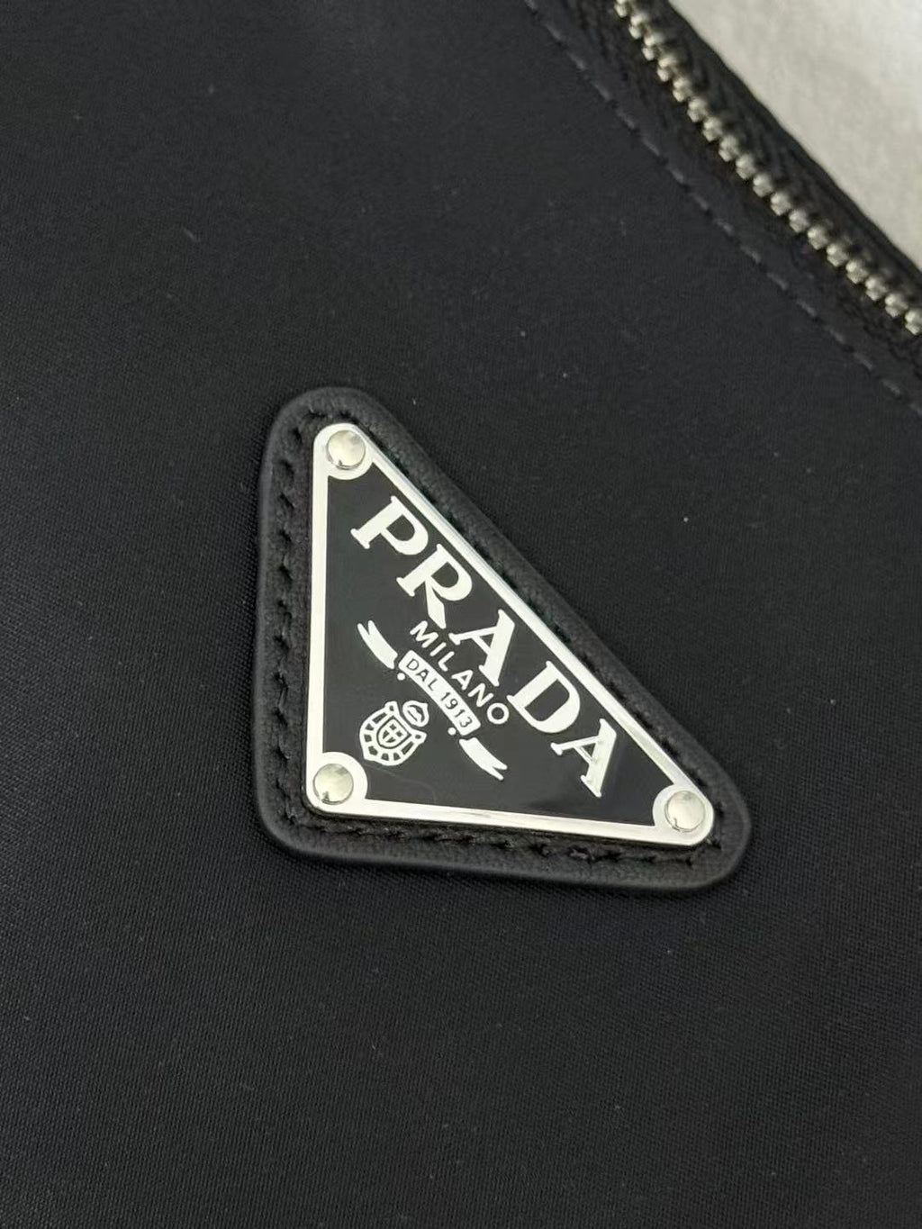 Prada logo patch on dark nylon with stitched border and triangular design