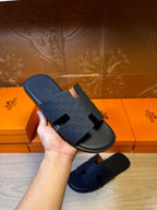 Hand holding blue slide sandals with wide cross strap and open toe