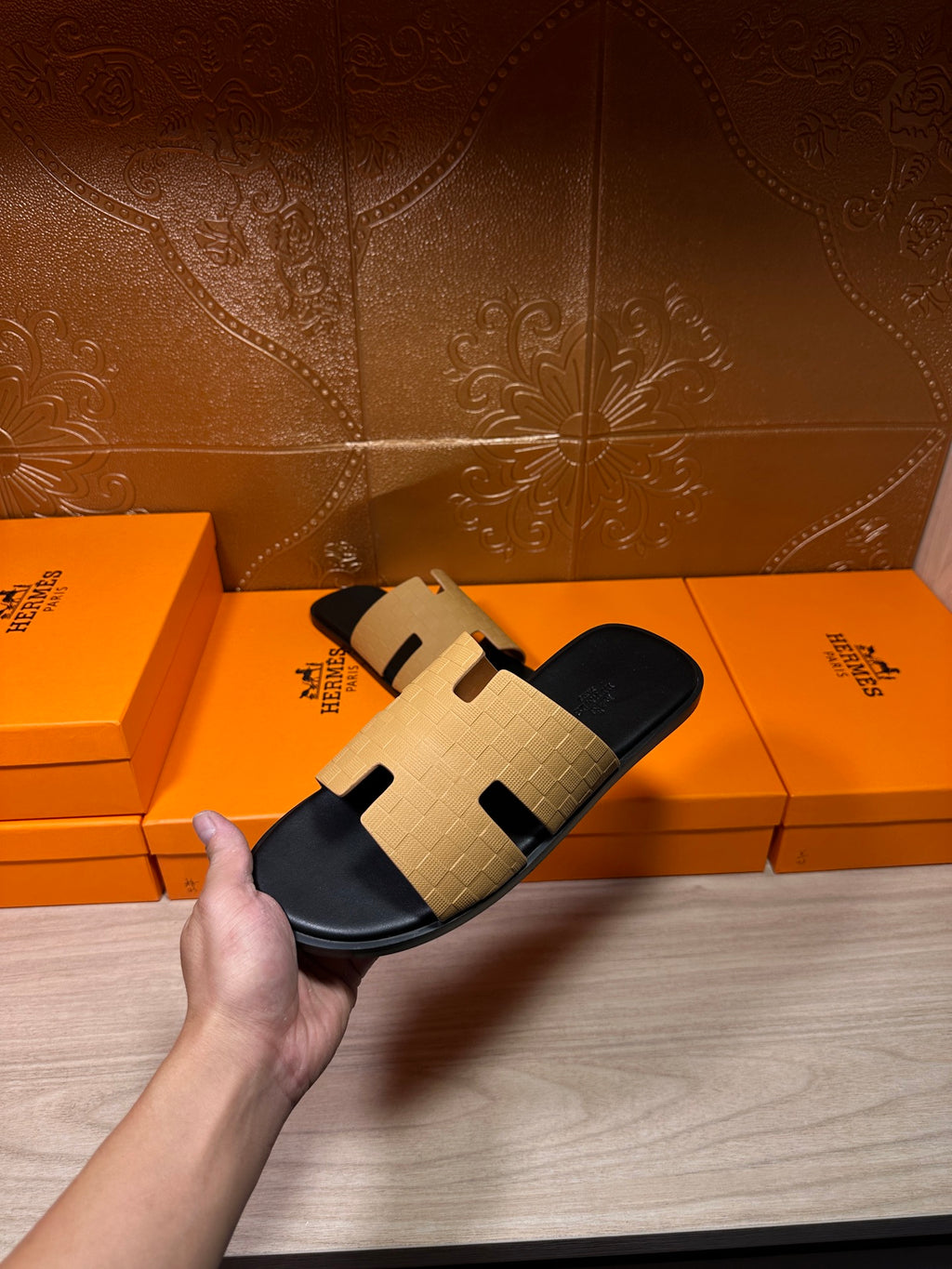 Hermes beige and black slide sandal held above box, open toe