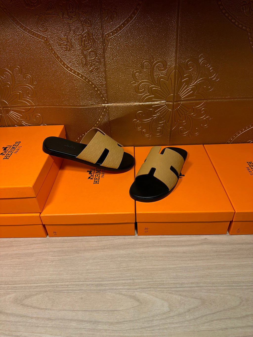 Hermes beige and black slide sandals, front view on stacked orange boxes