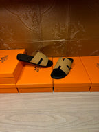 Hermes beige and black slide sandals, front view on stacked orange boxes