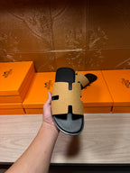 Hermes beige and black slide sandal held up, textured strap panels