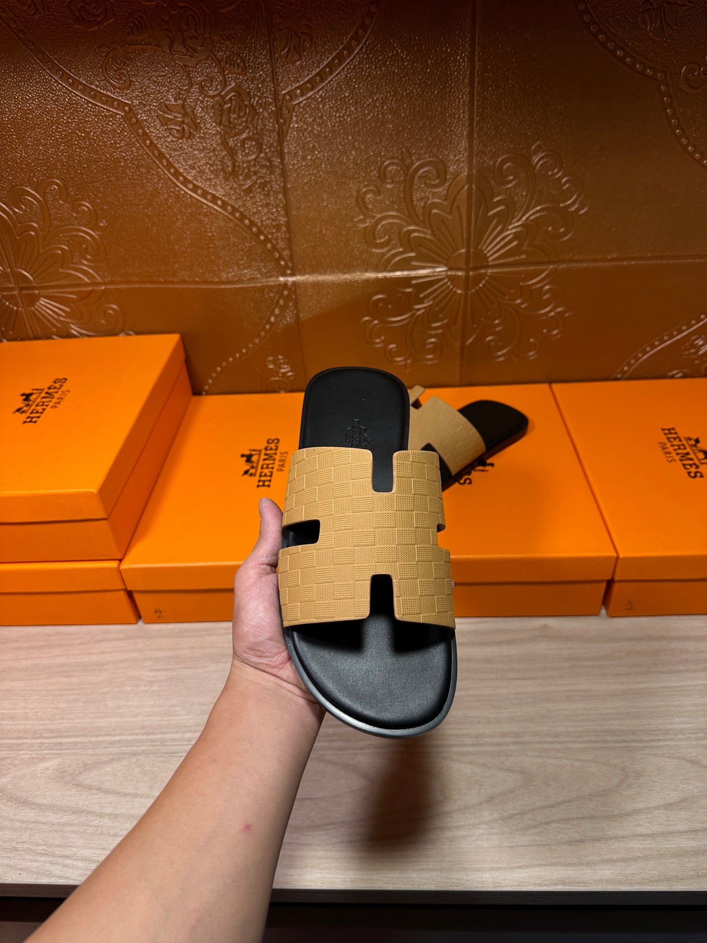 Hermes beige and black slide sandal held up, textured strap panels