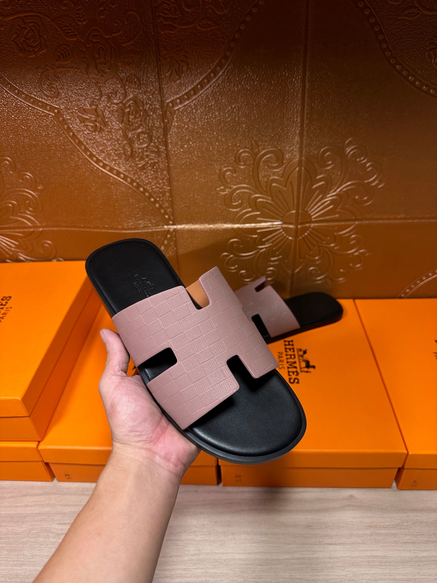 Hand holding a black slide sandal with light gray wide strap and open-toe design