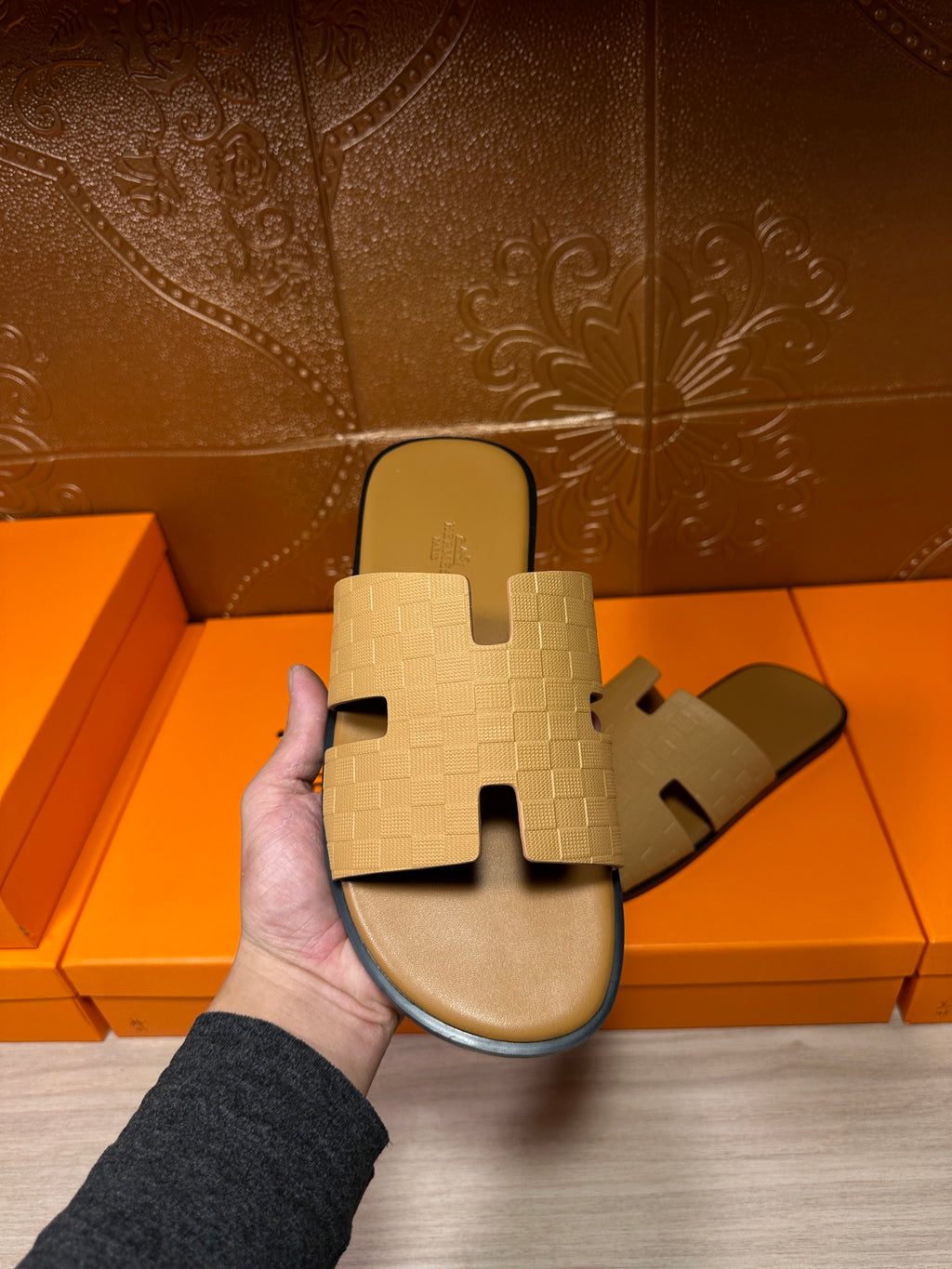 Beige slide sandals held in front of shoeboxes, open toe cross straps
