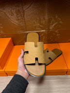 Beige slide sandals held in front of shoeboxes, open toe cross straps