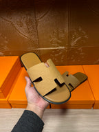 Beige slide sandal held up by hand, textured cross-strap upper