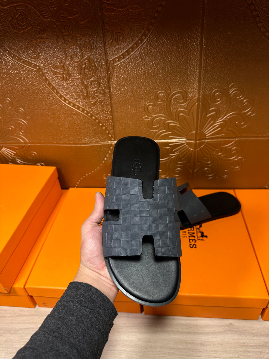 Hermes slide sandal held up, dark blue textured strap with molded H top