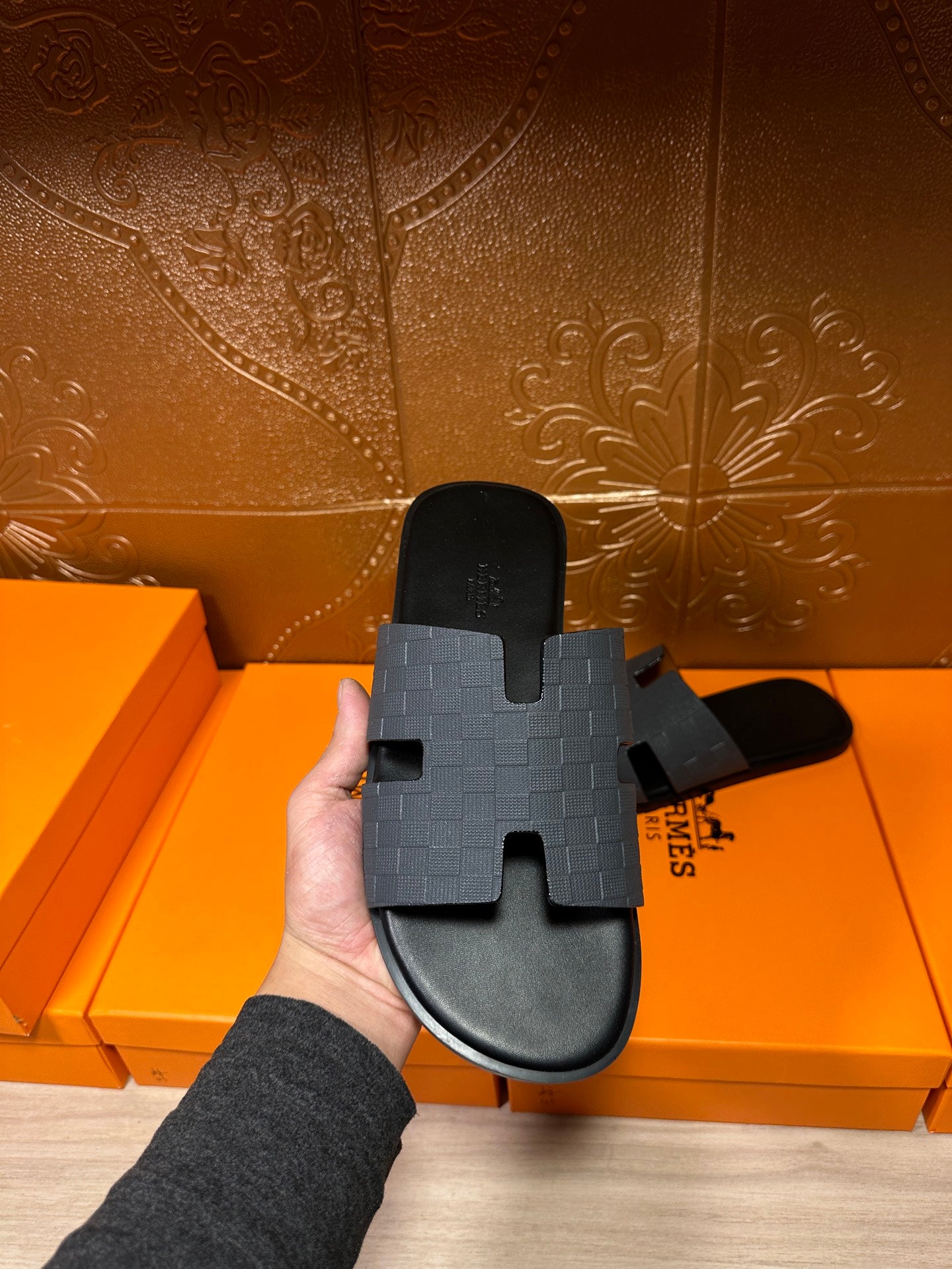 Hermes slide sandal held up, dark blue textured strap with molded H top
