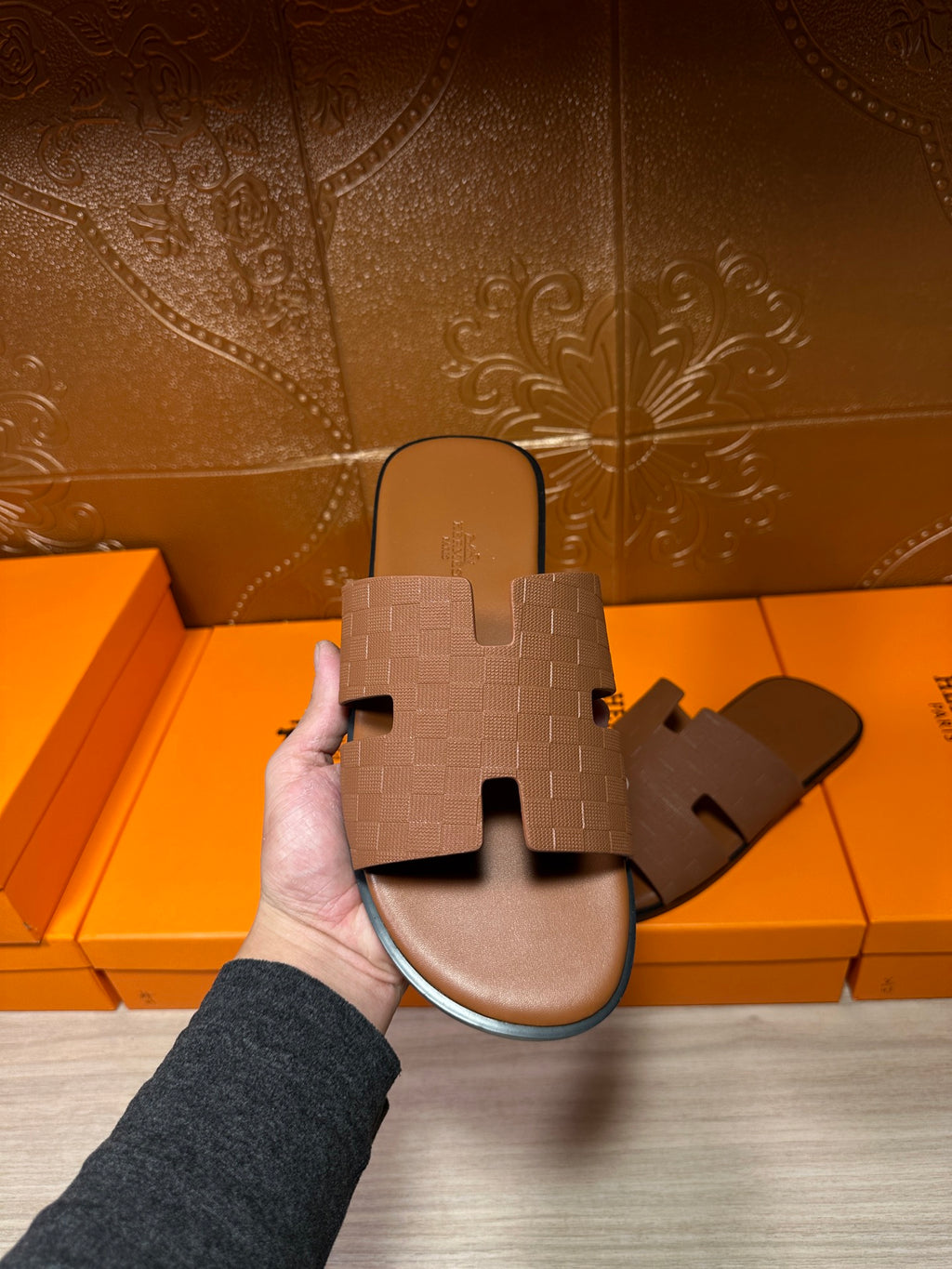 Hermes tan slide sandal with embossed strap, held in hand; open-toe slide design