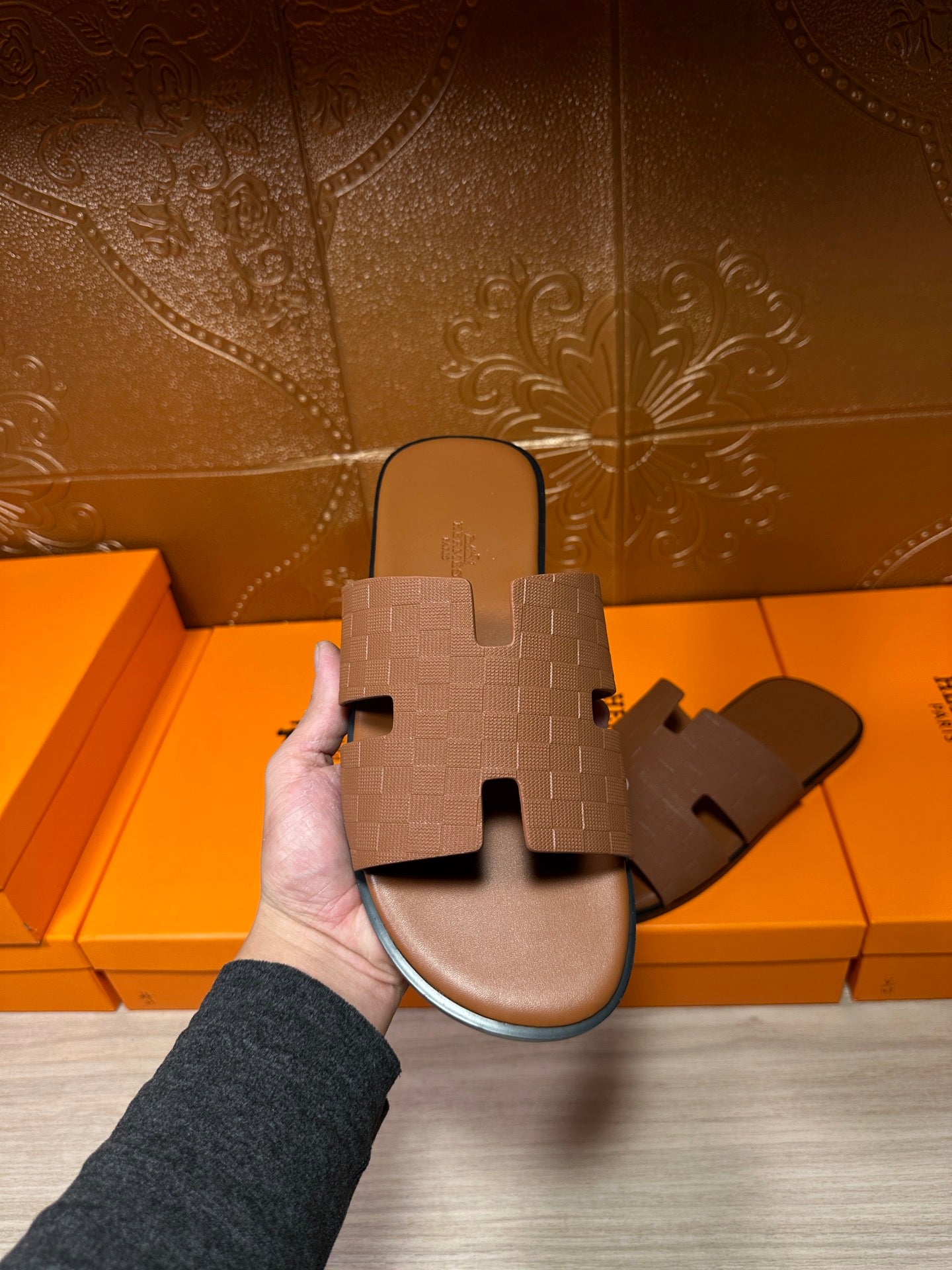 Hermes tan slide sandal with embossed strap, held in hand; open-toe slide design