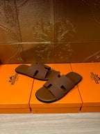 Hermes tan slide sandals with embossed strap, shown on top of orange retail boxes