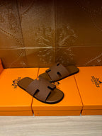 Hermes slide sandals with tan straps and open-toe cutouts on retail box