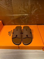 Hermes slide sandals with tan braided-look straps and open toe, shown as a pair on box