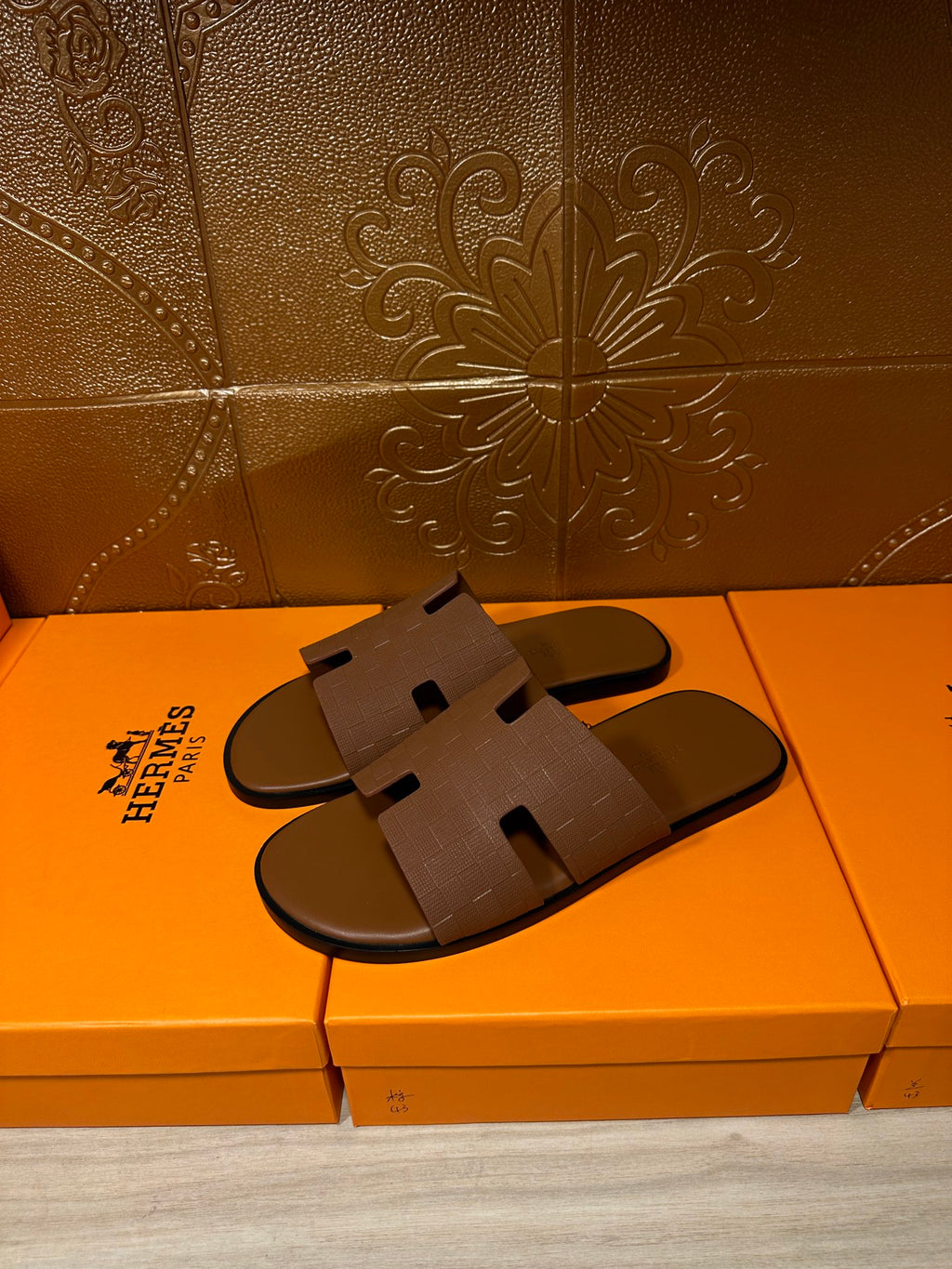 Hermes slide sandals with tan strap and cutout detail, side view on retail box
