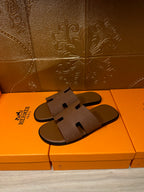 Hermes slide sandals with tan strap and cutout detail, side view on retail box