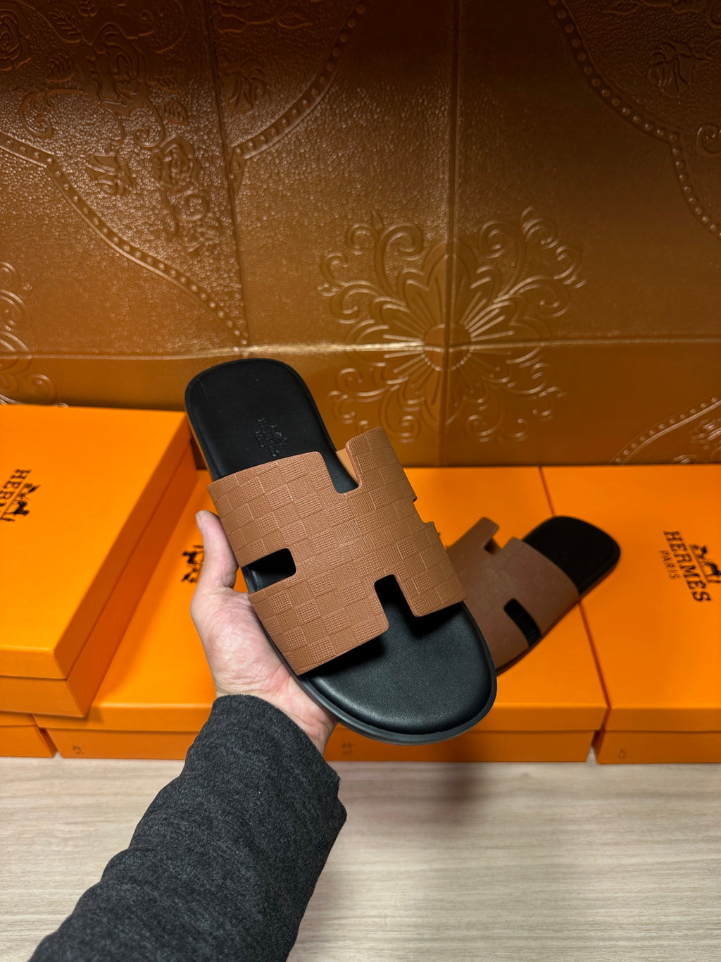 Tan leather slide sandal held in hand; black footbed and H-style strap